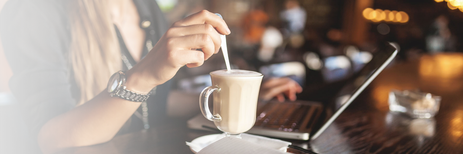 Image showing a close up of a woman in a coffee shop using her laptop whilst stirring her coffee