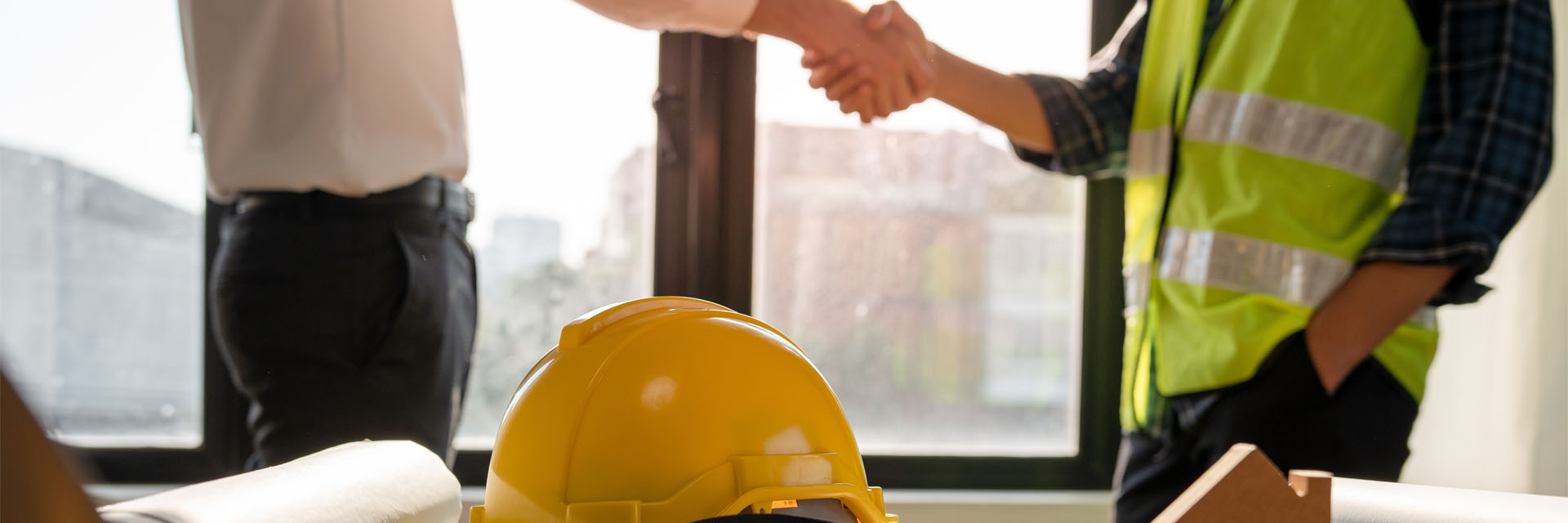 Image showing a close up of two men shaking hands, one wearing a high vis vest with a hard hat in front