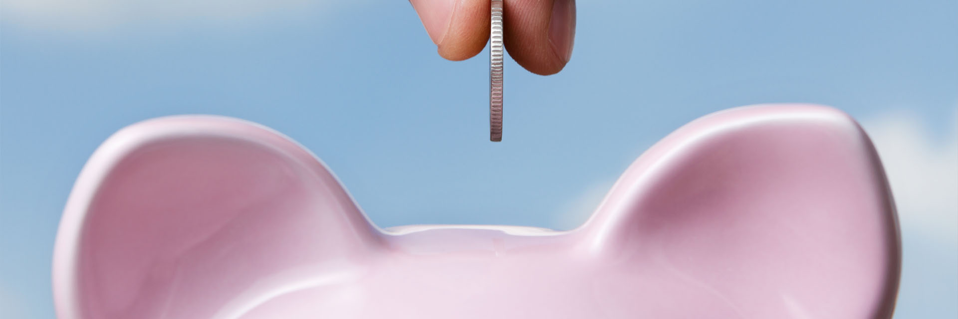 Image showing a close up of hand putting a coin in a piggy bank