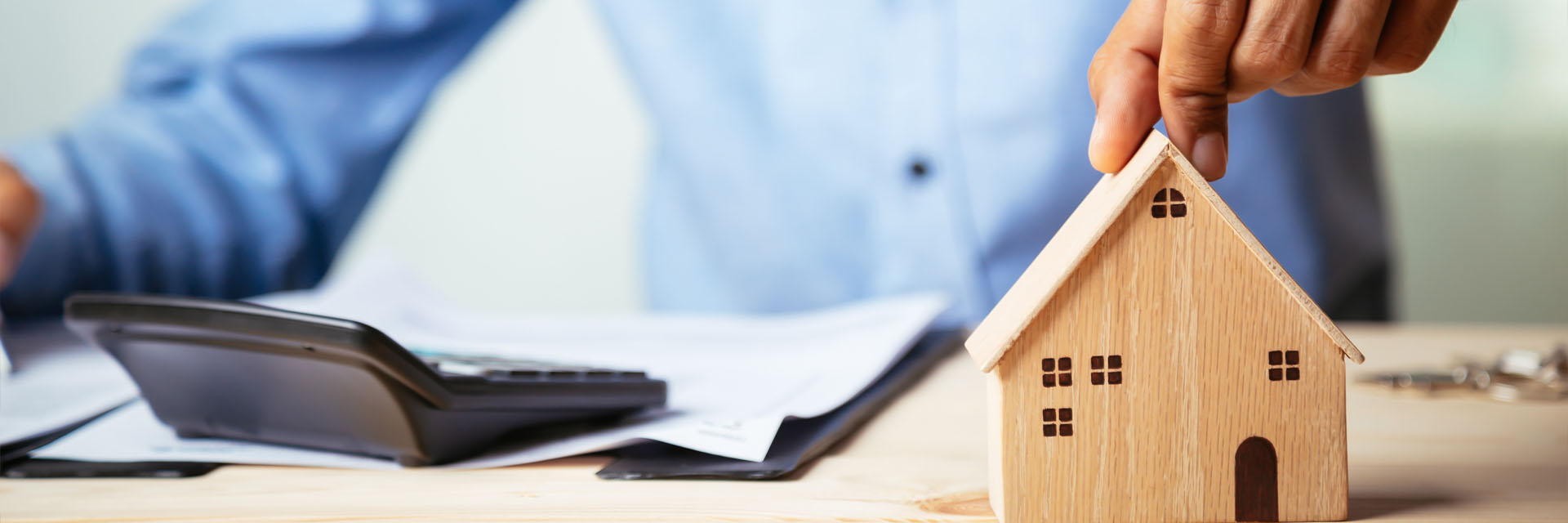 Image showing a close up of a man at his desk with some paperwork and a calculator and a hand on top of a model house