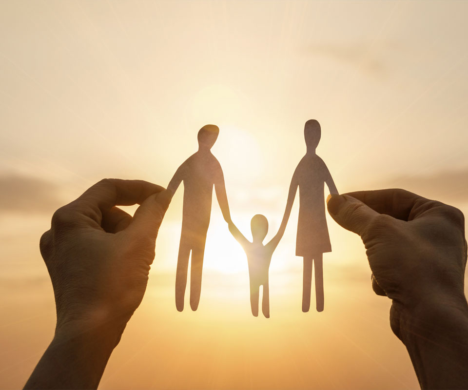 Image showing a close up of a set of hands holding up a paper cut out of a family during sunset