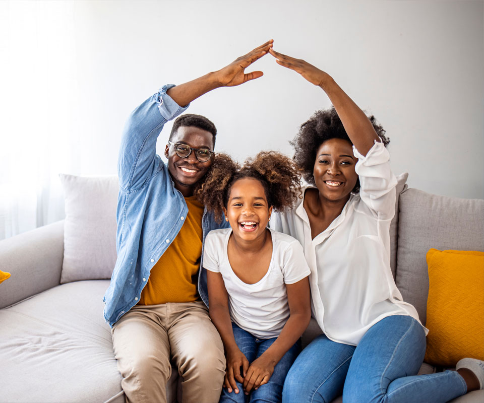 Image showing a smiling family sitting on their sofa holding their hands up like a roof over them