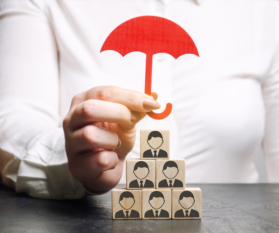 Image showing a close up of some building blocks with business men on them being protected by a woman holding a paper umbrella
