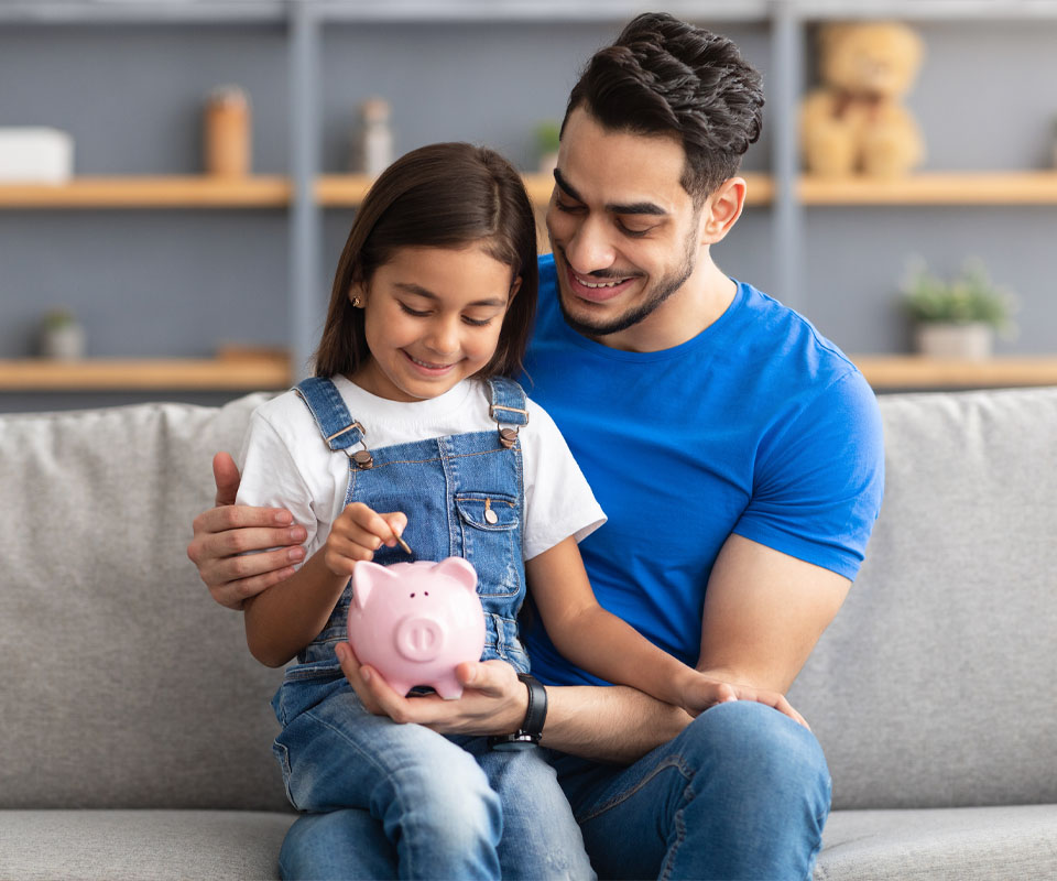 Image showing a Dad helping his daughter put a coin in a piggy bank