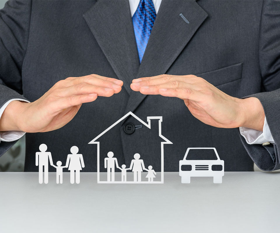 Image showing a close up of a man in a suit holding his hands over paper cut outs of a family, a house and a car to protect them