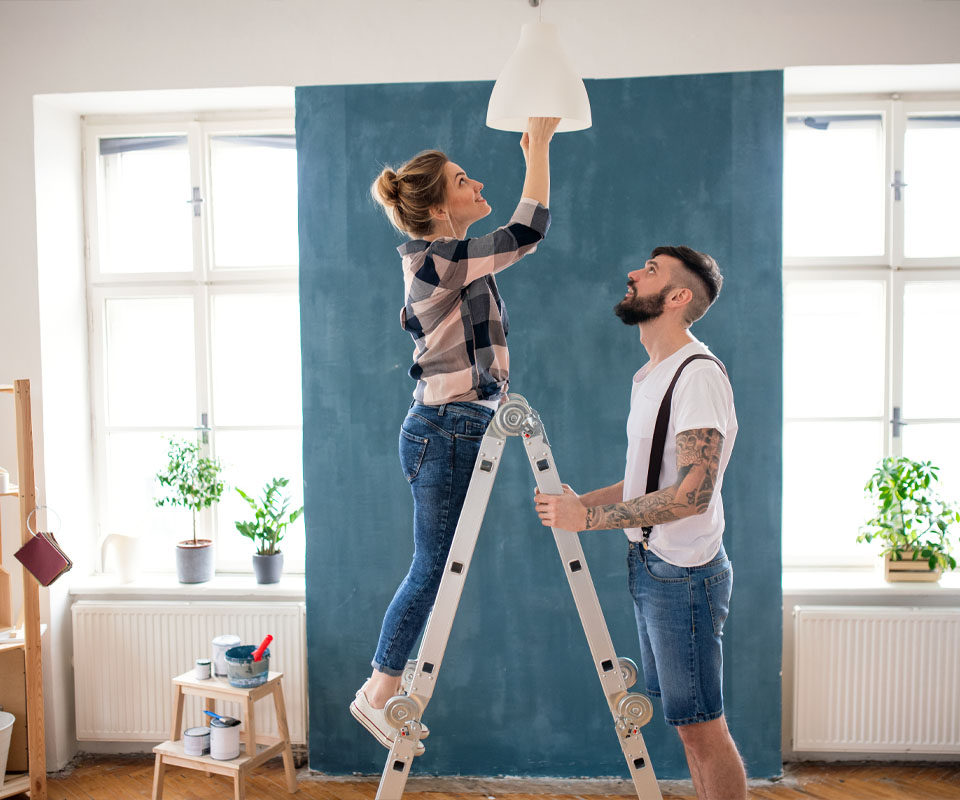 Image showing a man holding a ladder while a woman stands on it to put in a lightbulb