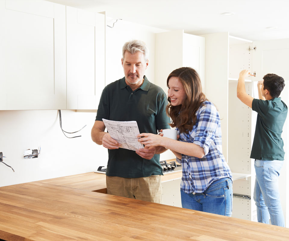 Image showing a couple looking at some plans in a kitchen being renovated with someone working in the background