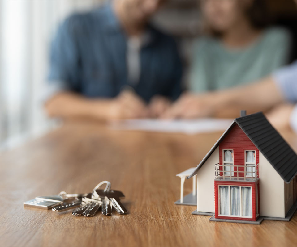 Image showing a close up of a model house and some keys with a meeting taking place in the background