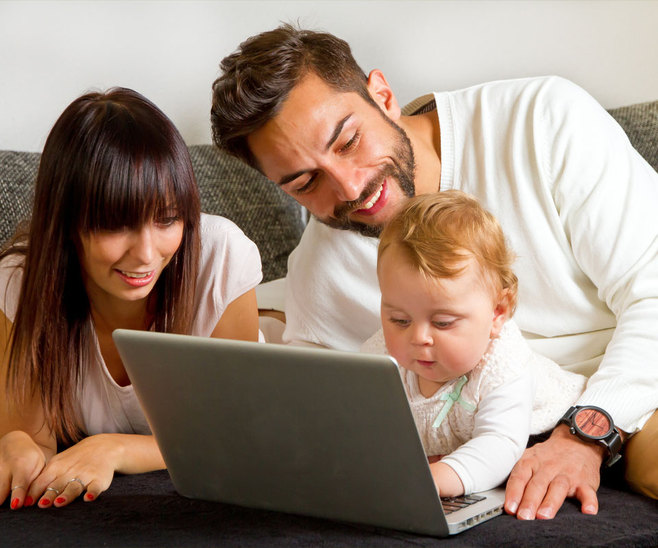 Image showing a couple on the sofa with their baby looking at a laptop