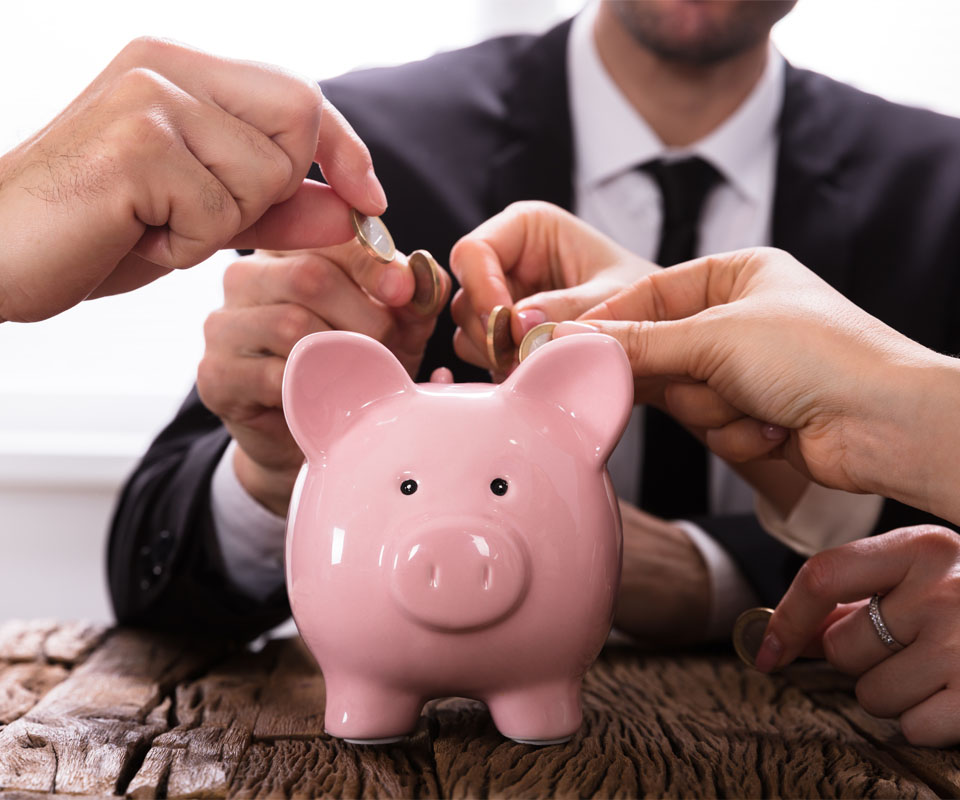 Image showing a close up of some business people putting coins in a piggy bank